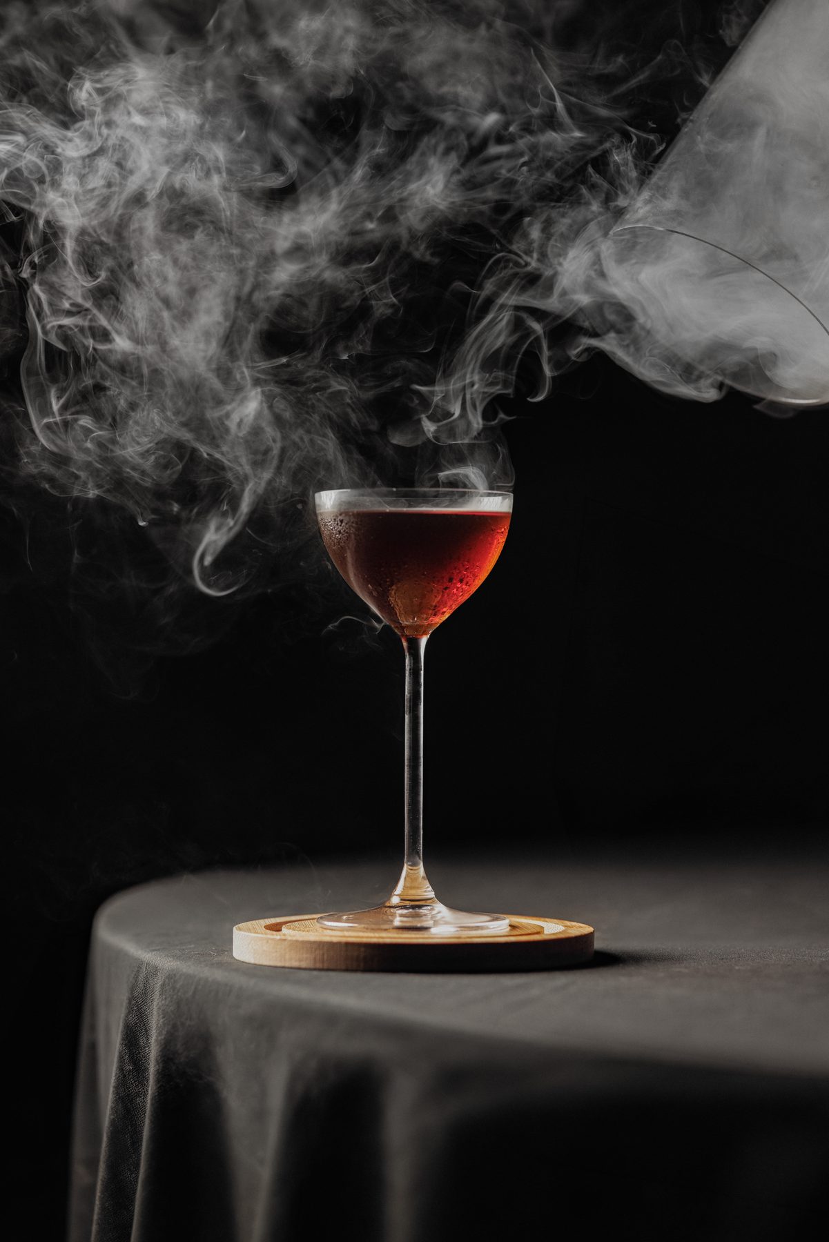 Cóctel Cvmclave entre humo sobre mesa con mantel negro